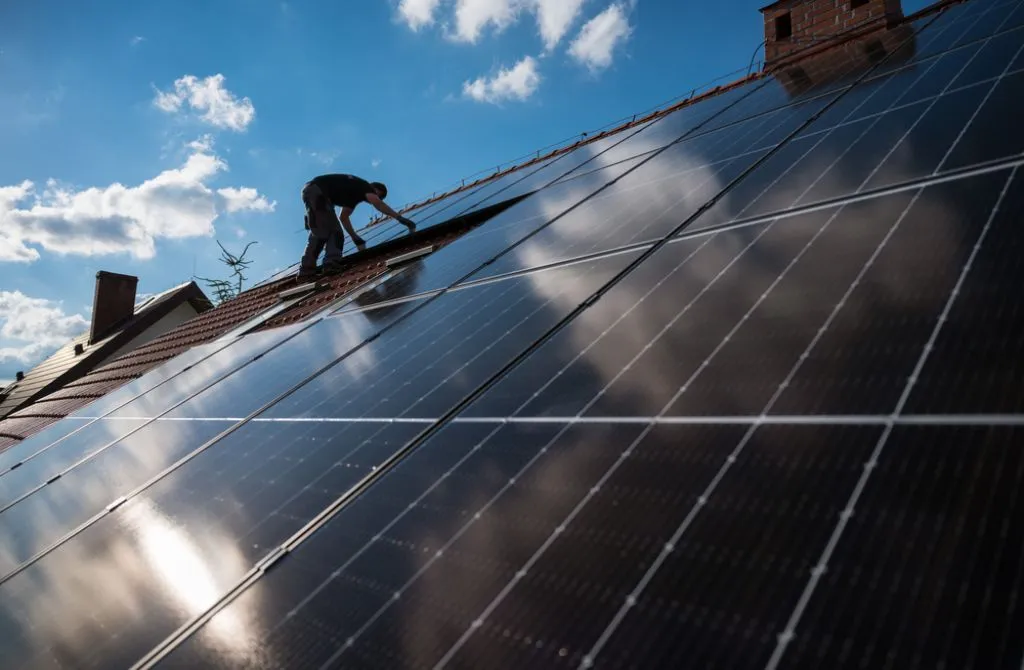 Solar technician mounting solar panels on a house roof.