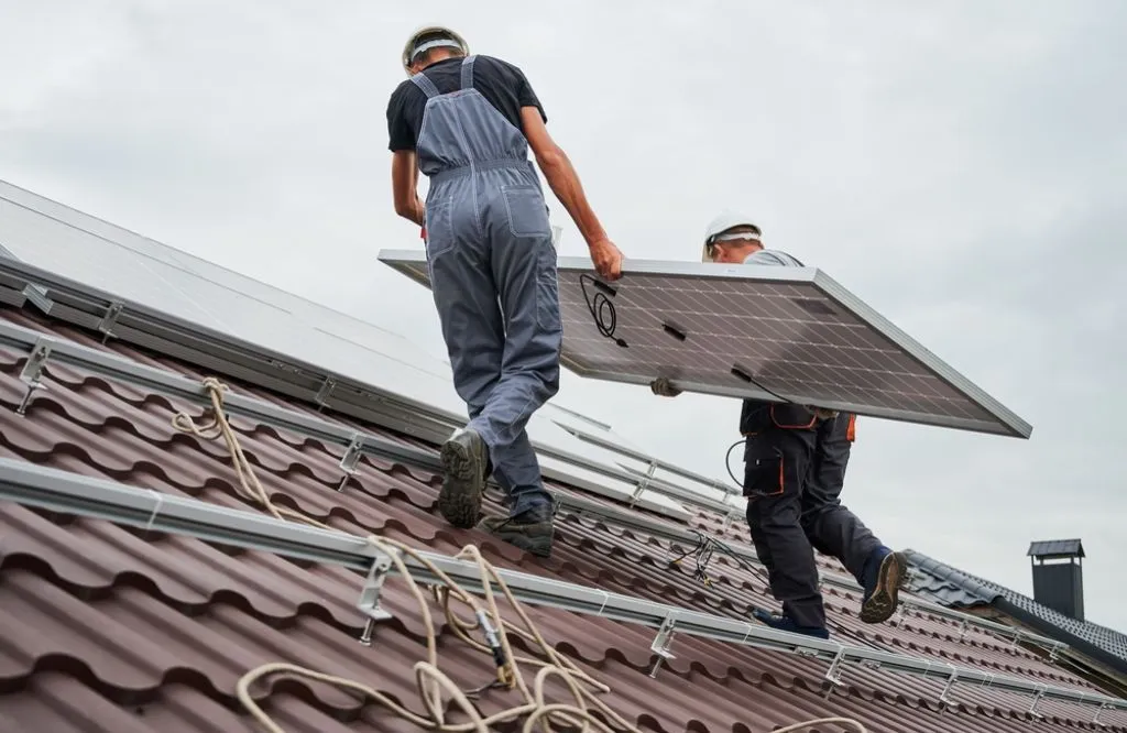 Men technicians carrying photovoltaic solar panels on the roof of the house.