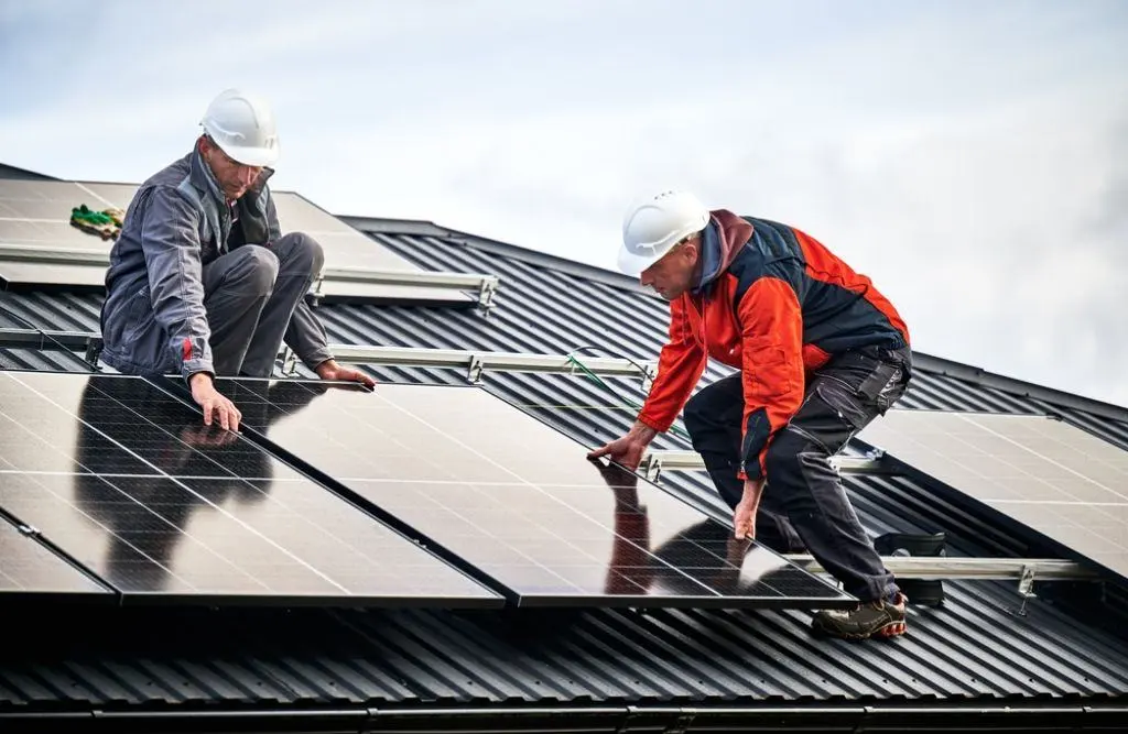  Technicians building photovoltaic solar module station on roof of house