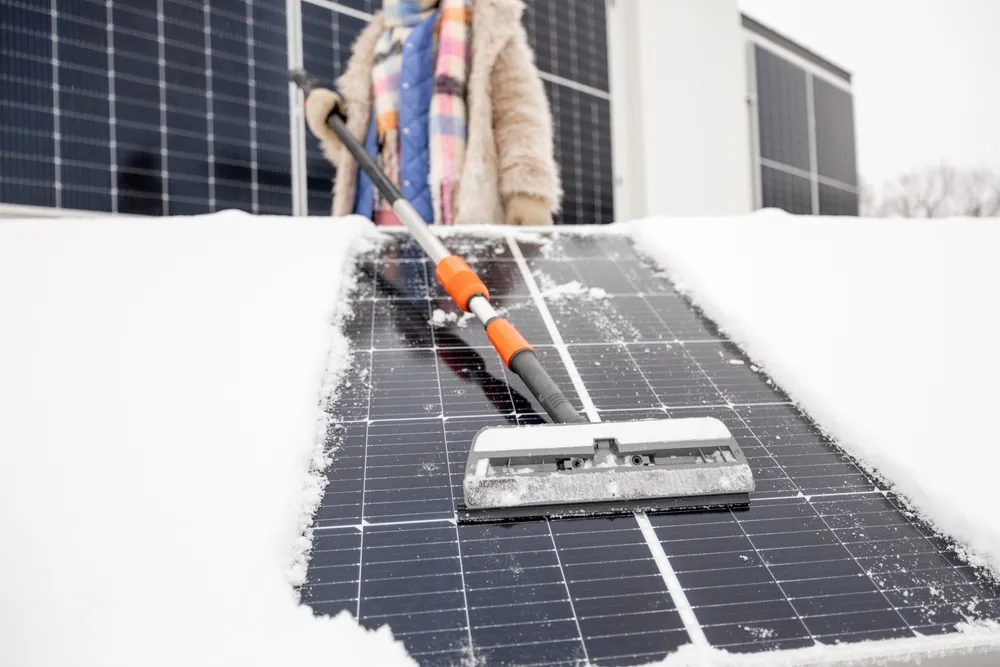Woman cleans solar panels from snow on the roof of her house.