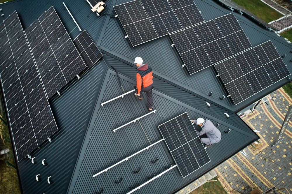 Aerial view of two male technicians installing photovoltaic solar panels on the house roof.
